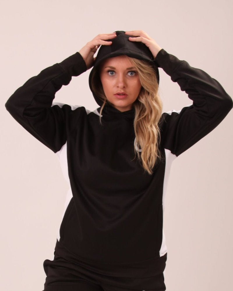 "Woman relaxing in UNIFY women's track pants, black with white stripes, showcasing casual yet chic styling."