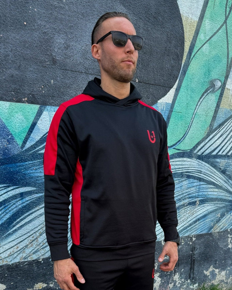 Detailed view of UNIFY black track pants with red side stripes, highlighting the fabric quality and stripe detail.