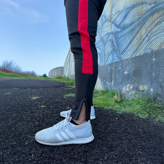 UNIFY Men's Crossover Track Pants in black with vibrant red stripes, shown during a dynamic workout.