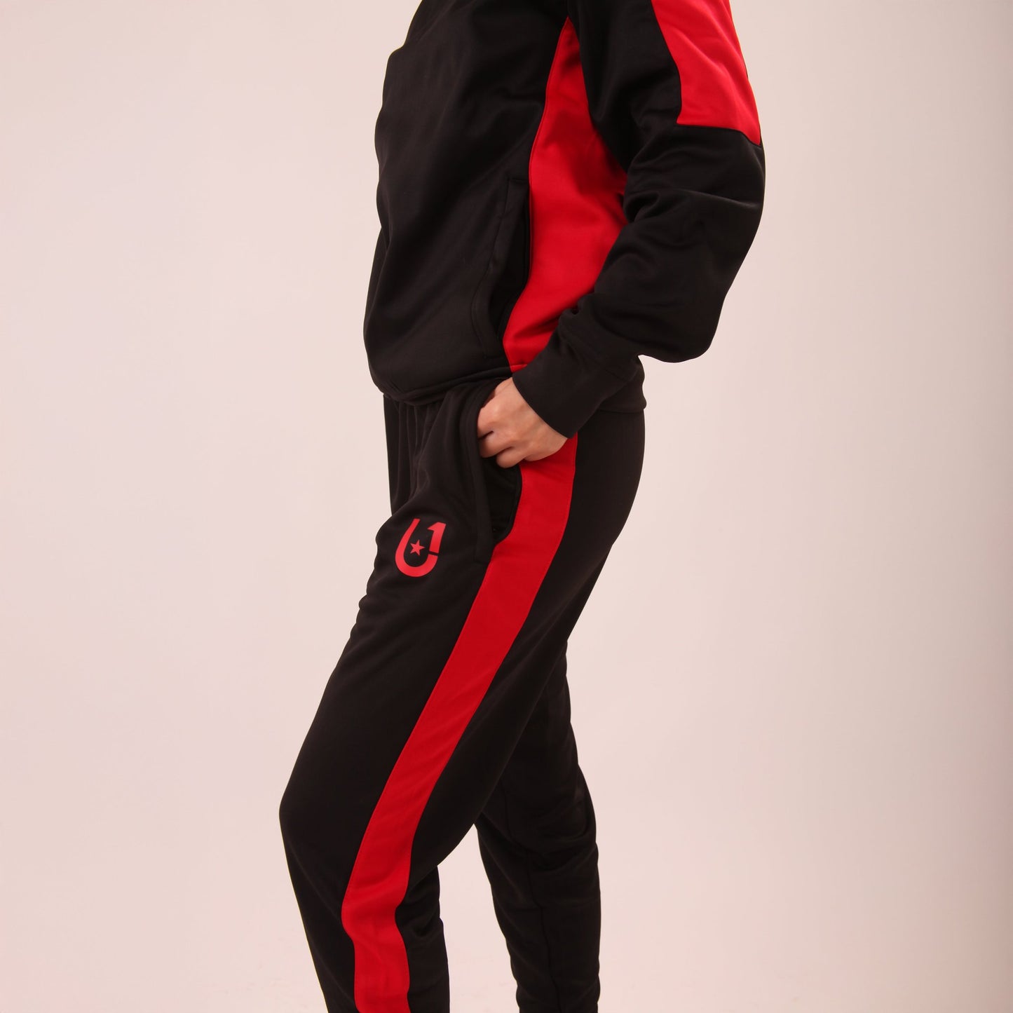 "Woman walking in UNIFY Women's Crossover Track Pants, showcasing the black fabric with bold red stripes."