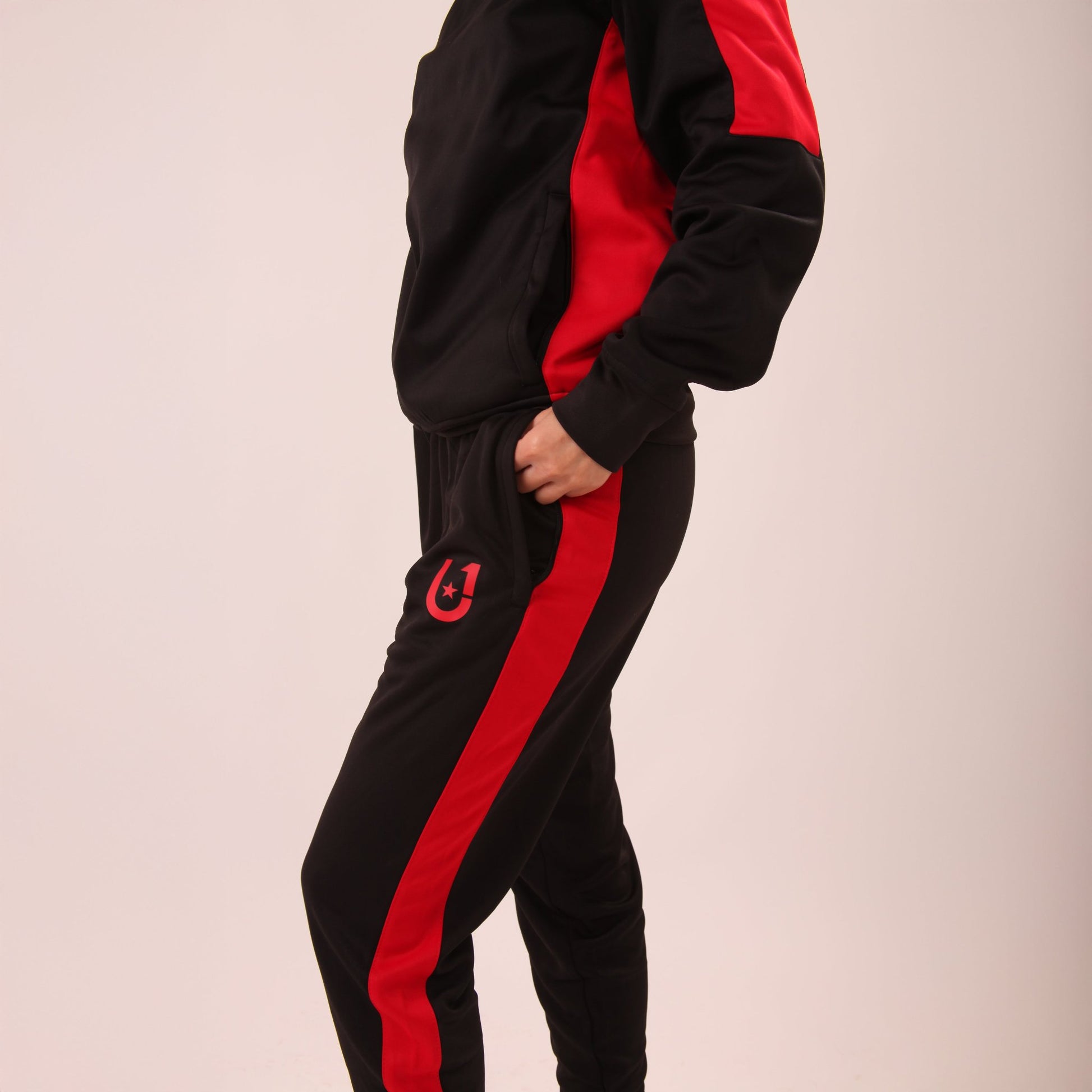 "Woman walking in UNIFY Women's Crossover Track Pants, showcasing the black fabric with bold red stripes."