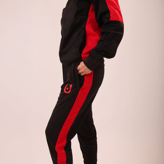 "Woman walking in UNIFY Women's Crossover Track Pants, showcasing the black fabric with bold red stripes."
