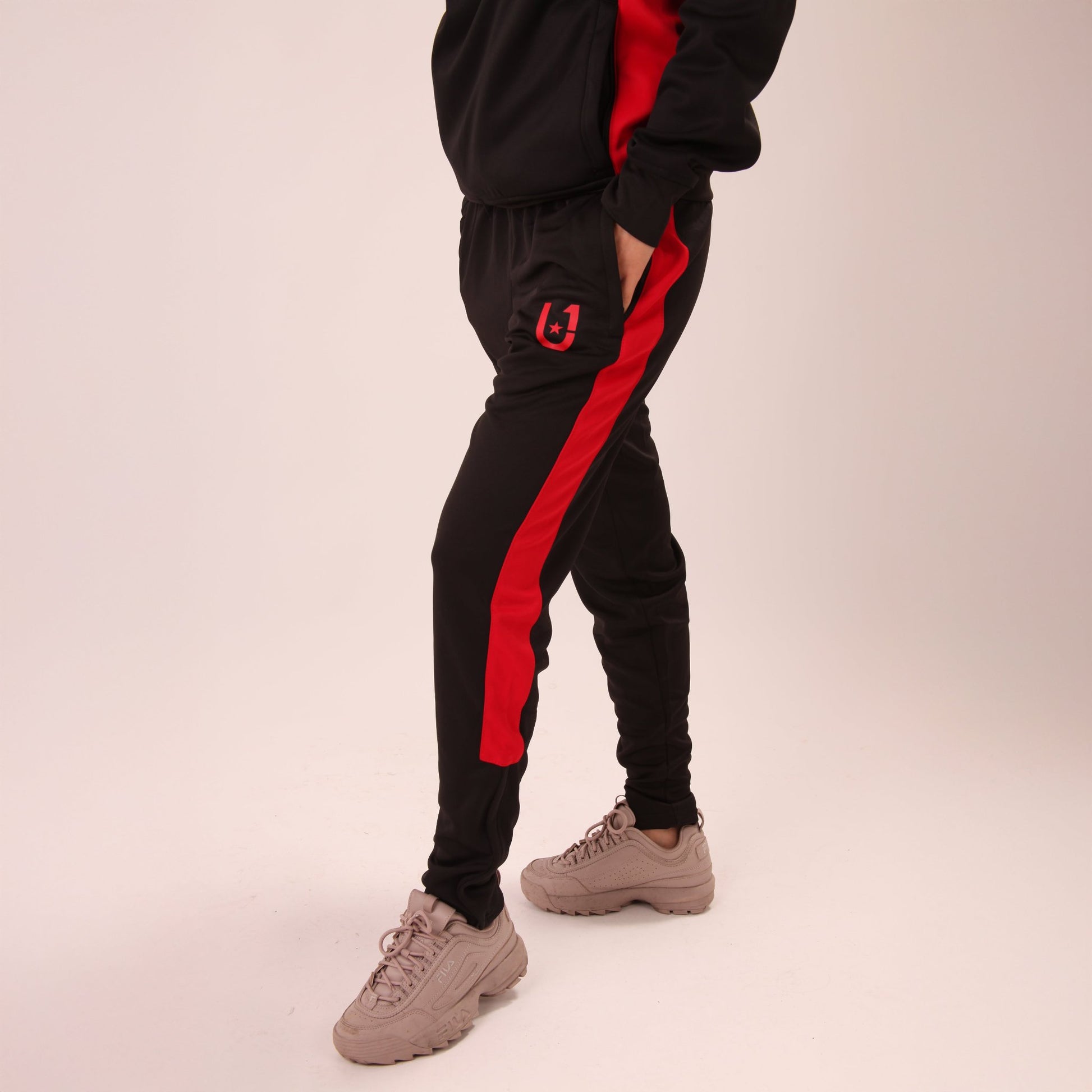 "Active shot of a woman stretching in UNIFY black and red stripe track pants, emphasizing comfort and mobility."
