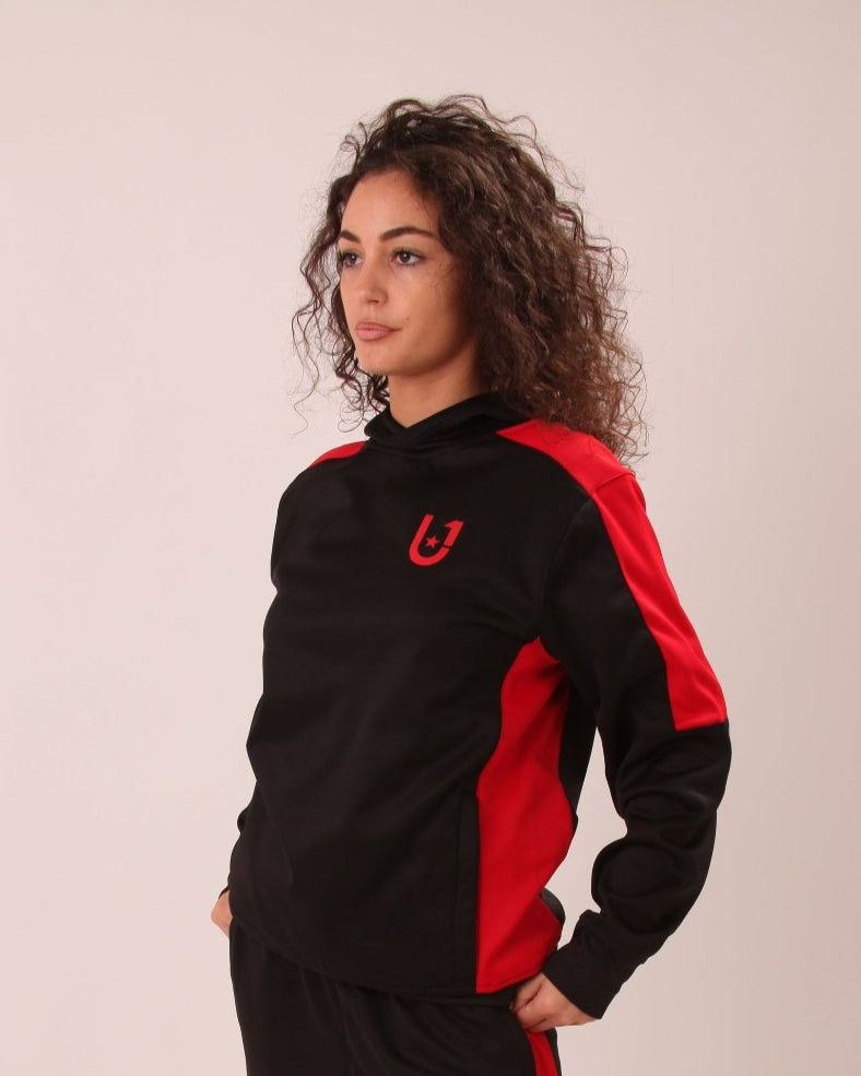 "Close-up view of UNIFY women's black track pants with red side stripes, focusing on the sleek design and stripe detail."
