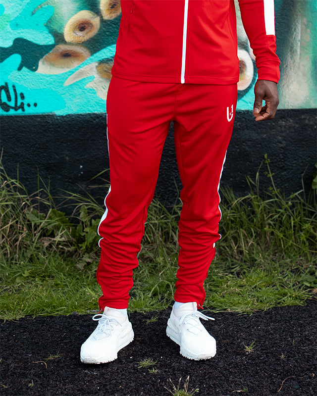 Red track pants with white side stripes styled for streetwear