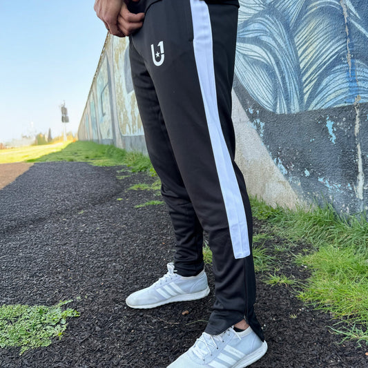 "Close-up of UNIFY men's track pants showing the sleek black fabric and contrasting white stripes, designed for a sharp look."
