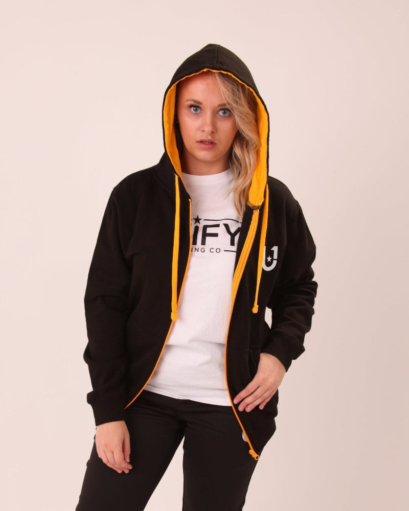 Woman sporting a black and yellow UNIFY zip hoodie, blending casual style with athletic comfort.
